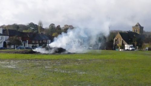 Smoldering remains of bonfire on village green next day with view of church